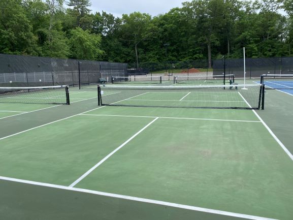 Four outdoor pickleball courts next to tennis court with fence in background